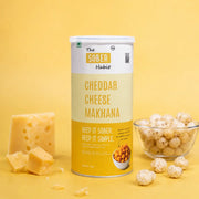 The Sober Habit Cheddar Cheese flavoured roasted makhana 70g canister with cheese blocks and fox nuts on yellow background
